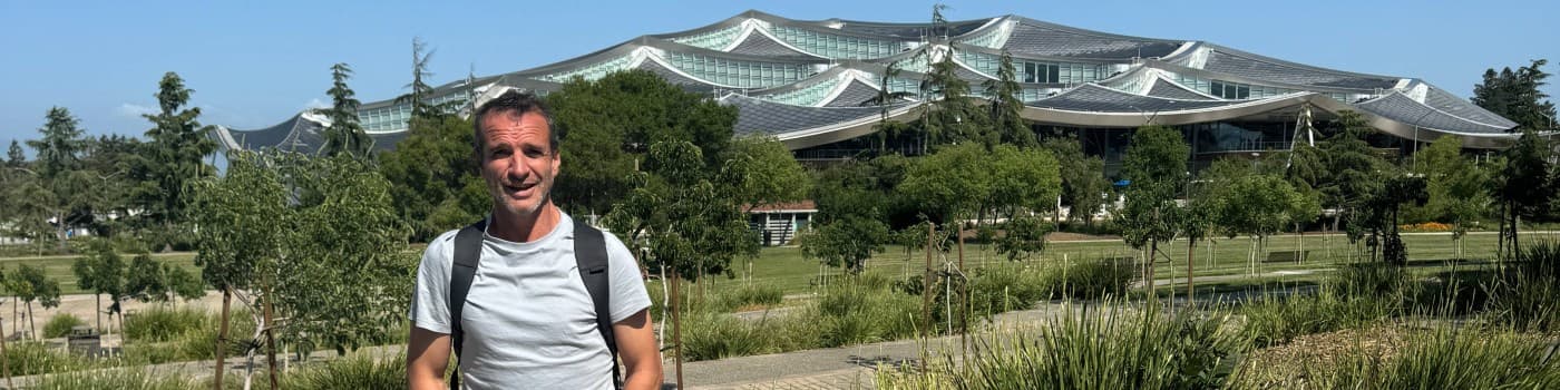 Fernando Errandosoro al aire libre, con mochila, frente a un edificio de techos ondulados rodeado de jardines.